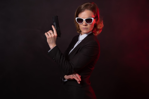 Geschäftsfrau mit einer Waffe in der Hand. Porträt auf einer schwarzen Wand
