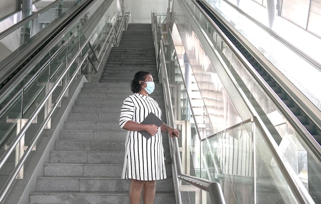 Geschäftsfrau mit Gesichtsmaske, die auf der Treppe steht und hinausschaut