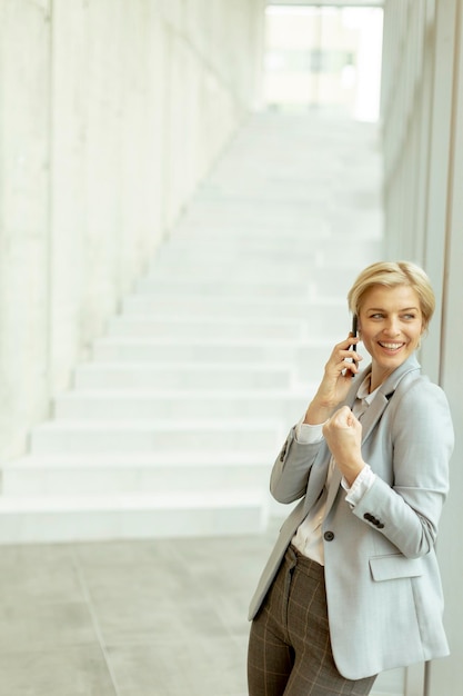 Geschäftsfrau mit Handy auf modernen Büroflur