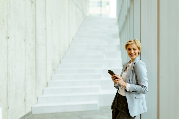 Geschäftsfrau mit Handy auf modernen Büroflur