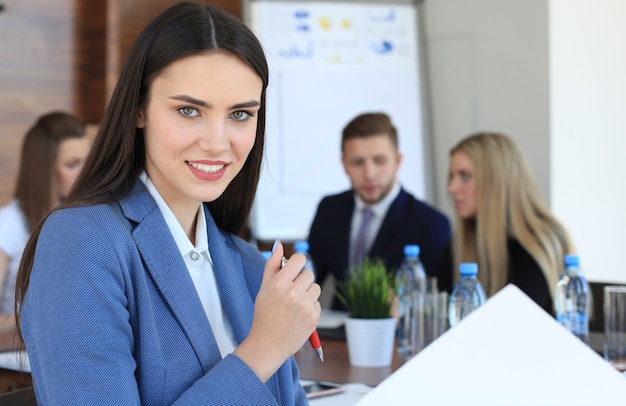 Geschäftsfrau mit ihrem Personal, Leutegruppe im Hintergrund im modernen hellen Büro im Innenbereich.