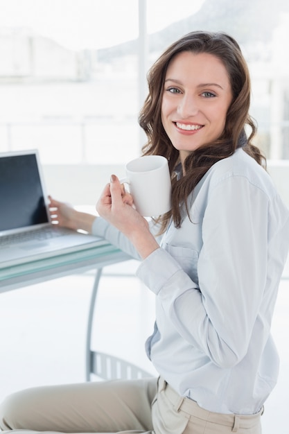 Geschäftsfrau mit Kaffeetasse vor Laptop im Büro