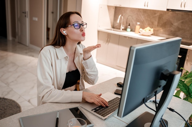 Geschäftsfrau mit Kopfhörern, die Freizeitkleidung tragen und zu Hause am Laptop arbeiten Junge glückliche Studentin, die an der Online-Universität studiert und per Videoanruf mit Freunden spricht