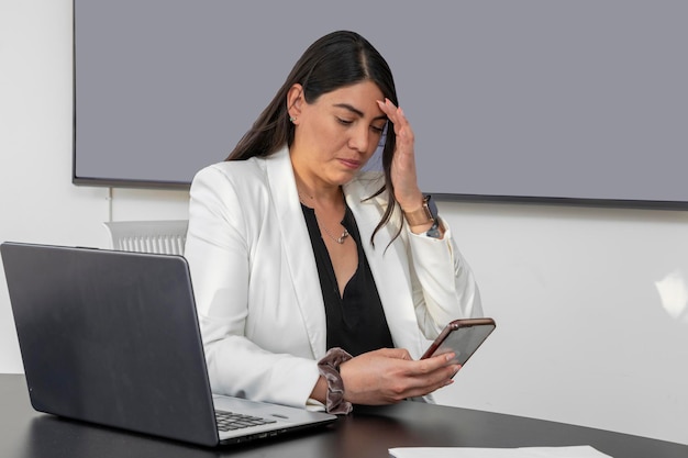 Geschäftsfrau mit Kopfschmerzen durch Arbeitsstress überprüft ihr Handy im Büro Executive Woman gestresst bei der Arbeit