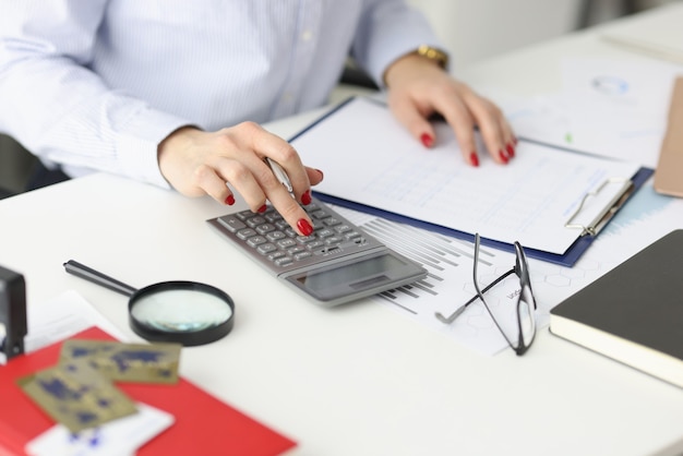 Geschäftsfrau mit roter Maniküre, die auf Taschenrechner in der Büronahaufnahmeberechnung von a zählt