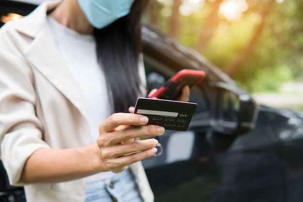 Geschäftsfrau mit Smartphone und Kreditkarte zum Online-Shopping im Auto. Neues normales Geschäftskonzept nach dem Ausbruch des Covid-19-Coronavirus.