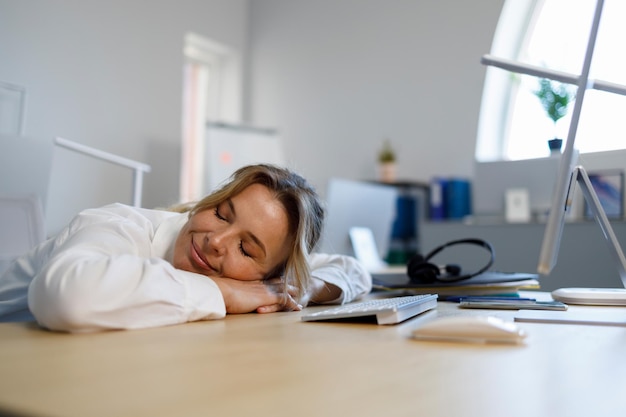 Geschäftsfrau mittleren Alters, die direkt am Arbeitsplatz ein Nickerchen macht