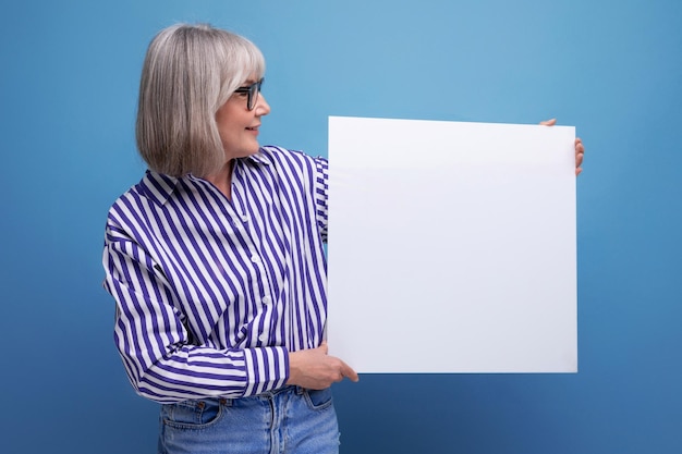 Geschäftsfrau mittleren Alters, die leere Plakatwand mit Attrappe auf hellem Studiohintergrund zeigt