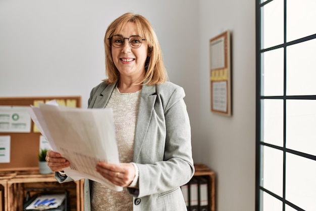 Geschäftsfrau mittleren Alters lächelt glücklich und hält Papierkram im Büro