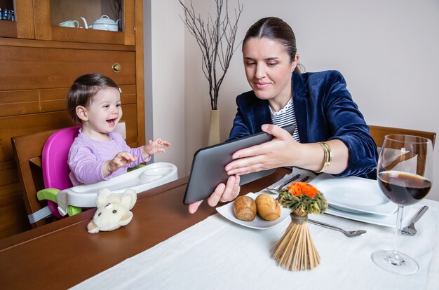 Geschäftsfrau Mutter und glückliches Baby Mädchen suchen Tablet-Computer sitzen in einem Restauranttisch