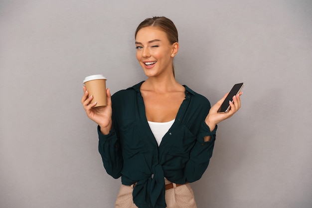 Geschäftsfrau posiert isoliert über grauem Wandhintergrund Kaffeetrinken mit Handy.