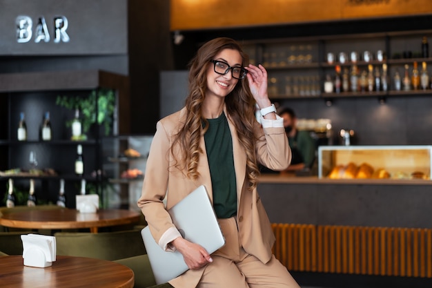 Geschäftsfrau Restaurantbesitzer mit Laptop in den Händen gekleidet eleganter Hosenanzug im Restaurant mit Bartheke Hintergrund kaukasischen weiblichen Brille Geschäftsperson Indoor stehen