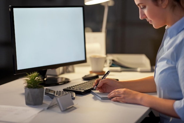 Geschäftsfrau schreibt nachts im Büro in ein Notizbuch