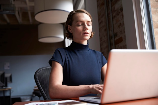 Geschäftsfrau sitzt am Schreibtisch am Fenster und arbeitet am Laptop