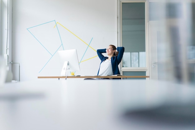 Geschäftsfrau sitzt am Schreibtisch in ihrem Büro, die Hände hinter dem Kopf