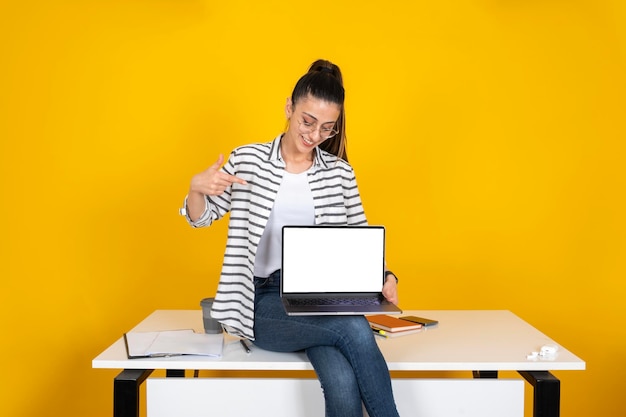 Geschäftsfrau sitzt auf dem Tisch und empfiehlt Website. Mädchen zeigt auf Laptop-Attrappe