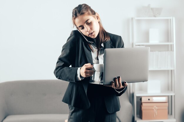 Geschäftsfrau sitzt drinnen im Büro mit Laptop-Computer im Büro Beschäftigter Büroangestellter trinkt Kaffee am Telefon mit Laptop-Computer