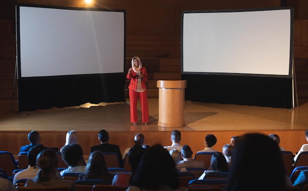 Geschäftsfrau steht in der Nähe des Podiums und hält dem Publikum eine Präsentation