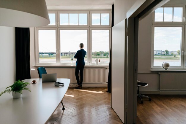 Geschäftsfrau steht in einem modernen Büro und schaut aus dem Fenster