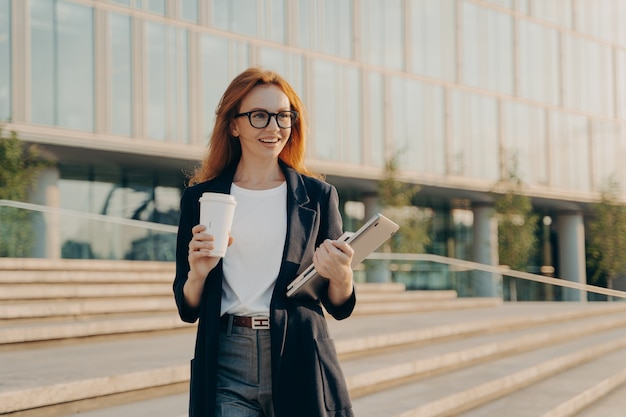 Geschäftsfrau trägt elegante formelle Kleidung Getränke zum Mitnehmen Kaffee trägt Notebook und modernes Gadget