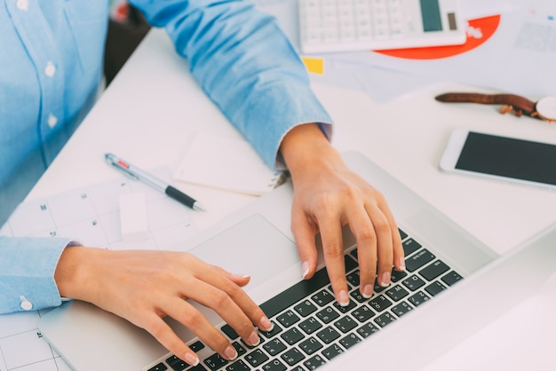 Geschäftsfrau übergibt das Schreiben der Laptoptastatur auf Schreibtisch mit Arbeitsplatz