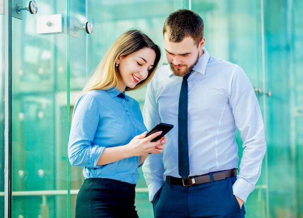 Geschäftsfrau und Geschäftsmann mit dem Mobiltelefon, das eine Arbeit planiert