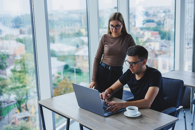 Geschäftsfrau und Geschäftsmann suchen etwas im Laptop Das Konzept der geschäftlichen Zusammenarbeit und Teamarbeit Junge lächelnde Millennials am Tisch im Büro Moderne erfolgreiche Menschen