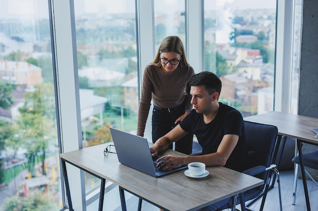 Geschäftsfrau und Geschäftsmann suchen etwas im Laptop Das Konzept der geschäftlichen Zusammenarbeit und Teamarbeit Junge lächelnde Millennials am Tisch im Büro Moderne erfolgreiche Menschen