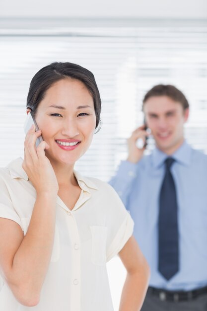 Geschäftsfrau und Mann, der Mobiltelefone im Büro verwendet