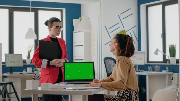 Geschäftsfrauen, die mit grünem Bildschirm auf dem Laptop im Startup-Büro arbeiten. Kollegen, die einen Computer mit Chroma-Key und isolierter Mock-up-Kopierraumvorlage auf leerer Hintergrundanzeige verwenden.