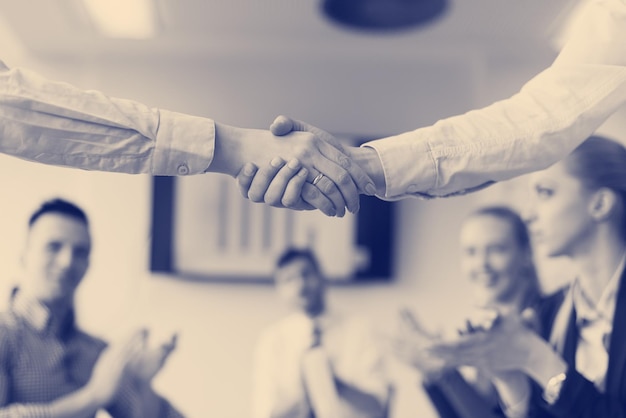 Geschäftsfrauen-Handschlag bei Teambesprechung mit einer Gruppe von Personen, die im Hintergrund im modernen Start-Business-Büro-Interieur verschwommen sind