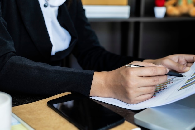 Geschäftsfrauen-Nahaufnahmehand mit Papierschreiben am Diagramm, unter Verwendung des Computer-Notizbuchlaptops und des Smartphone, Marketing-Geschäft für Erfolgs-Konzept.