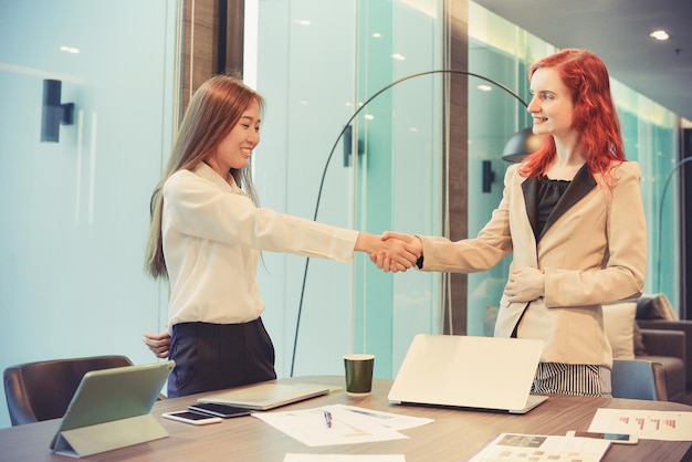 Geschäftsfrauen schütteln sich am Tisch im Büro die Hand