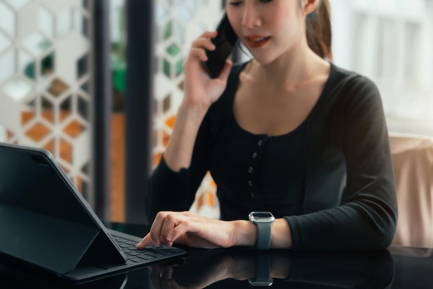 Geschäftsfrauen sprechen Mobiltelefone und verwenden ein Tastatur-Tablet, das Online-Geschäftsarbeit vom Heimtelearbeitskonzept aus bearbeitet