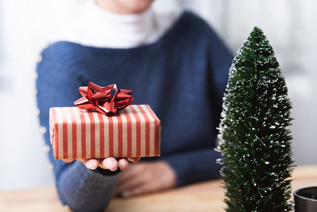 Geschäftsfrauhand, die Geschenkbox im Weihnachtsfeiertag im Büro mit Weihnachtsdeko hält