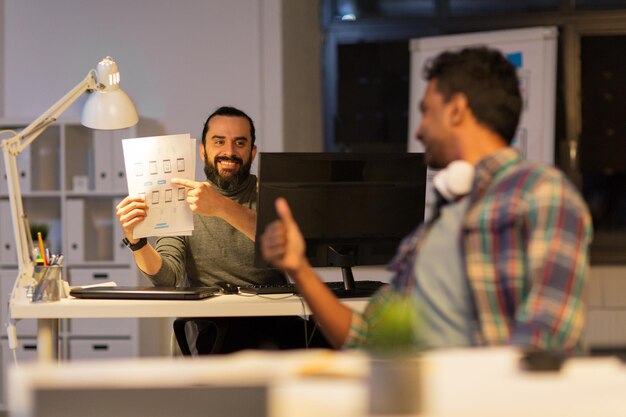 Foto geschäftsfrist und webdesign menschen konzept glücklicher kreativer mann zeigt papiere an kollegen im nachtbüro