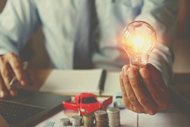 Geschäftshand, die Glühlampe mit dem Verwenden des Laptop- und Geldstapels im Büro hält