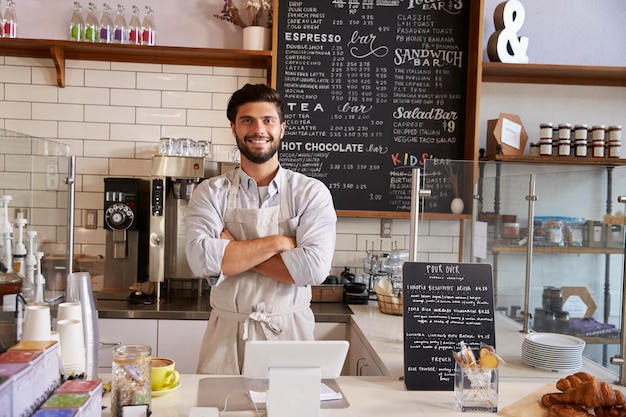 Geschäftsinhaber an der Theke eines Cafés mit gekreuzten Armen