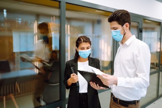 Geschäftskollegen, die eine medizinische Gesichtsmaske tragen, diskutieren gemeinsam über Arbeitsprobleme im Büro. Teamarbeit während der Pandemie in der Quarantänestadt. Covid19.