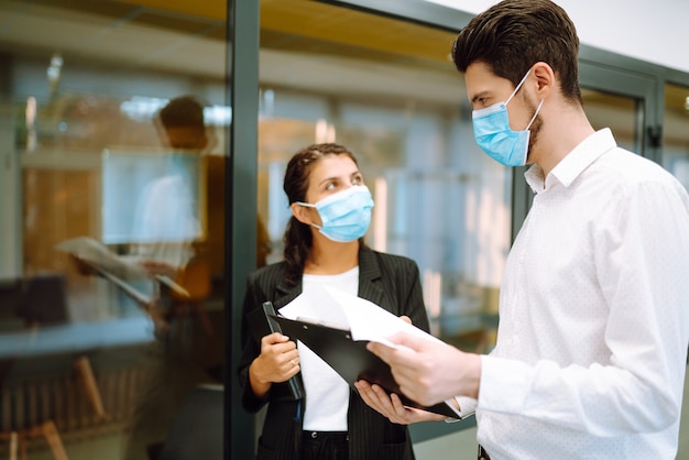 Geschäftskollegen, die eine medizinische Gesichtsmaske tragen, diskutieren gemeinsam über Arbeitsprobleme im Büro. Teamarbeit während der Pandemie in der Quarantänestadt. Covid19.