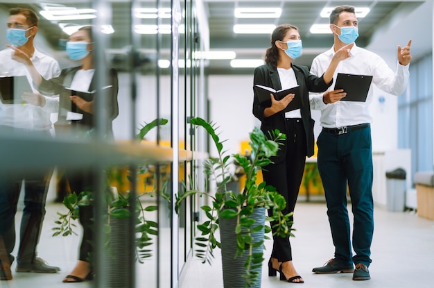 Geschäftskollegen, die eine medizinische Gesichtsmaske tragen, diskutieren gemeinsam über Arbeitsprobleme im Büro. Teamarbeit während der Pandemie in der Quarantänestadt. Covid19.