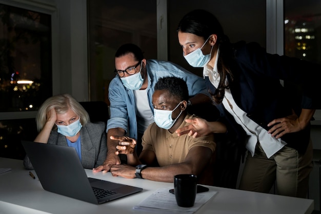 Geschäftskollegen, die spät im Büro arbeiten, während sie medizinische Masken tragen wearing