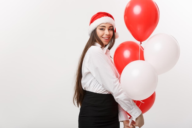 Geschäftskonzept Schöne junge, selbstbewusste Geschäftsfrau mit Weihnachtsmütze, die einen Ballon hält, feiern zu Weihnachten