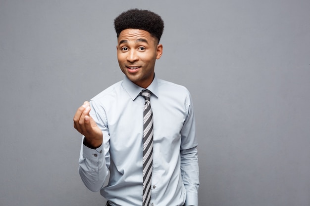 Geschäftskonzept - Selbstbewusster fröhlicher junger Afroamerikaner, der Hände vor ihm mit überraschendem Ausdruck über grauer Wand zeigt.