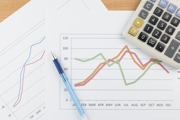 Geschäftskonzept: Taschenrechner und blauer Stift auf Diagrammhintergrund.
