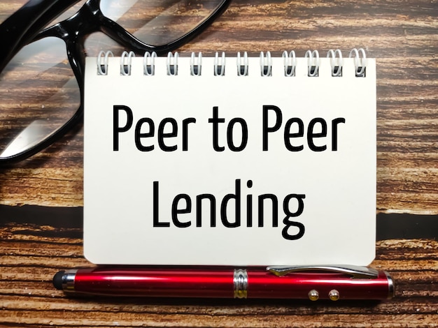 GeschäftskonzeptText Peer-to-Peer-Lending-Schreiben auf Notebook mit Brille und Stift auf Holzhintergrund