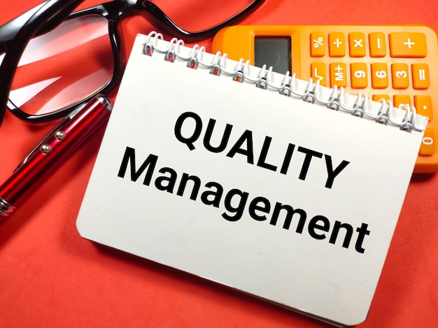 GeschäftskonzeptText Qualitätsmanagement auf Notebook mit Stiftbrille und Taschenrechner auf rotem Grund