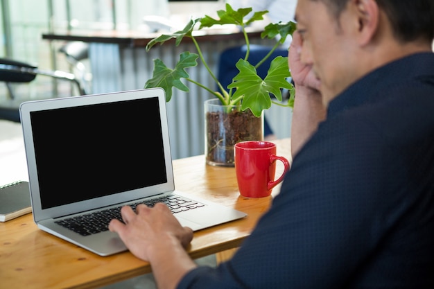 Geschäftsleiter, der am Schreibtisch sitzt und Laptop verwendet