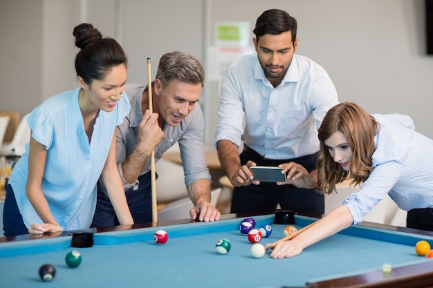 Geschäftsleiter, der Foto mit Handy macht, während Kollegen Billard spielen