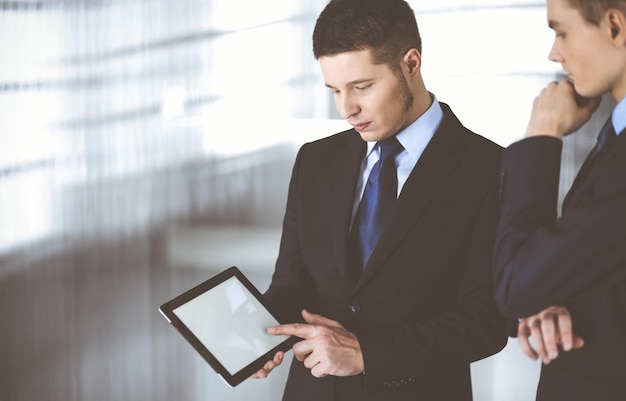 Geschäftsleute benutzen einen Tablet-Computer, während sie in einem modernen Büro stehen. Unbekannter Geschäftsmann mit einem Kollegen am Arbeitsplatz. Teamwork und Partnerschaftskonzept.